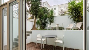 En terrasse med træterrasse, hvide stole, et bord og krukker med planter.