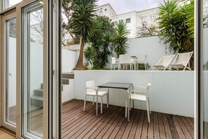Een terras met een houten dek, witte stoelen, een tafel en potplanten.