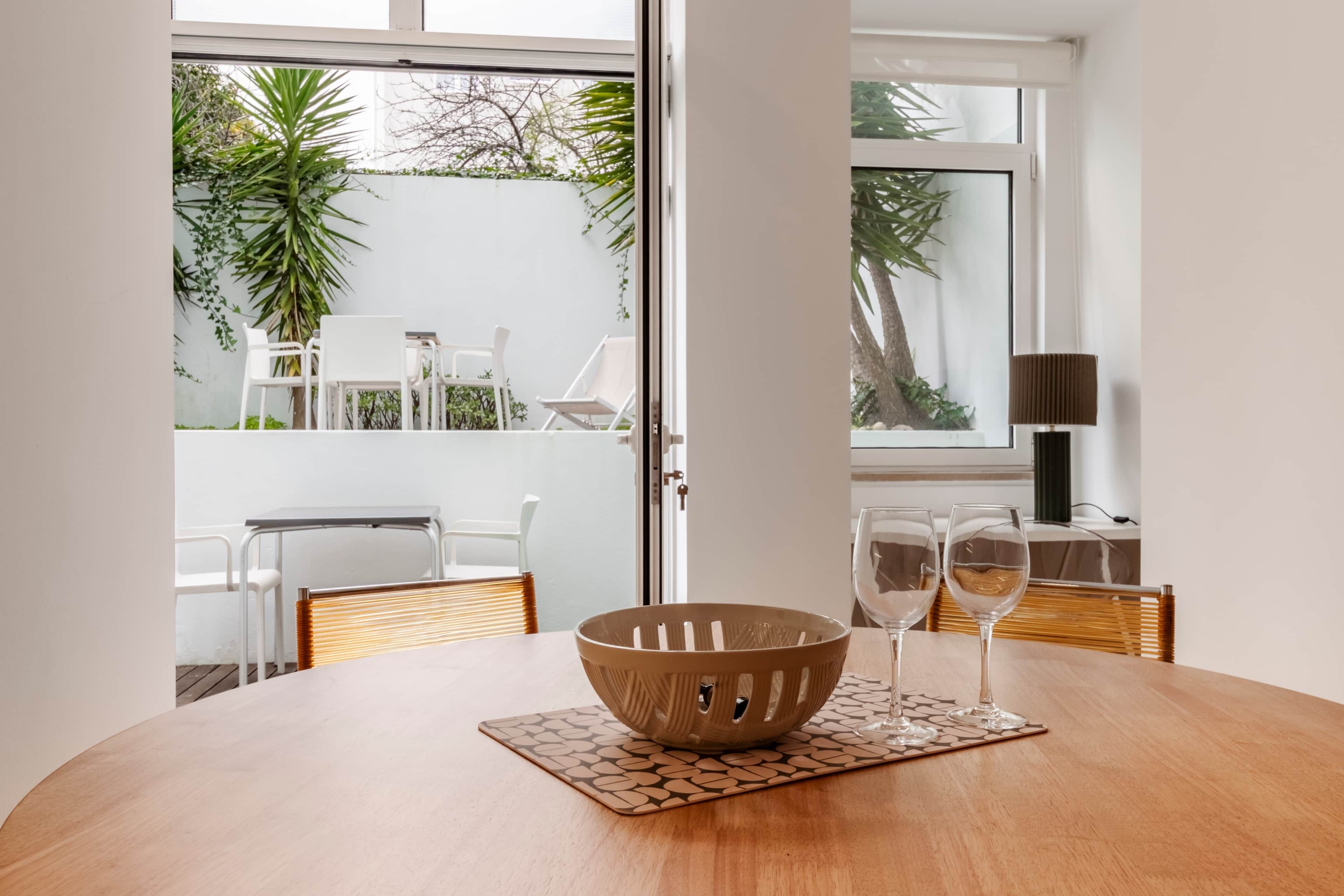 A dining area with a round table, a bowl, and two wine glasses on a mat.
