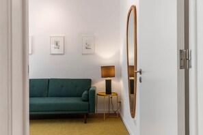 A room with a green sofa, a small table with a lamp, and two framed pictures on the wall. - Garden Terrace - Lisbon City Retreat (Lisboa)