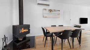 Ein modernes Wohnzimmer mit Kamin, einem Esstisch mit Stühlen, einem Wand-Fernseher und einem Gemälde mit Strandmotiv.