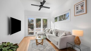 A modern living room with a sofa, a glass coffee table, a TV, and a ceiling fan.