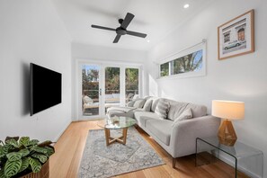 A modern living room with a sofa, a glass coffee table, a TV, and a ceiling fan.