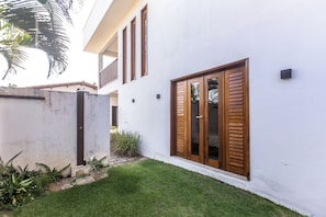 A modern building with a white exterior, large wooden shutters, and a well-maintained lawn. - Guesthouse Flamingo with 2 bedrooms and garden in the heart of Cumbuco (Caucaia)