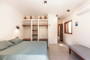 A bedroom with a bed, a wardrobe with shelves, a bench, and a door leading to another room. - Guesthouse Flamingo with 2 bedrooms and garden in the heart of Cumbuco (Caucaia)