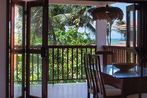 A room with a view of a beach and palm trees, a dining table with chairs, and a hanging light fixture. - Guesthouse Flamingo with 2 bedrooms and garden in the heart of Cumbuco (Caucaia)