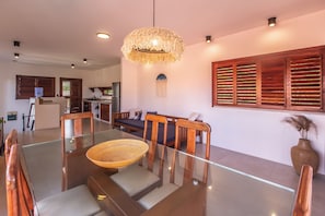 A modern dining area with a glass table, wooden chairs, and a woven light fixture. - Guesthouse Flamingo with 2 bedrooms and garden in the heart of Cumbuco (Caucaia)