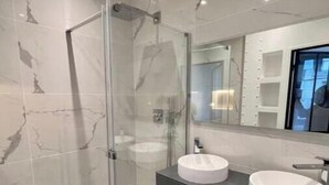 Un baño moderno con ducha acristalada, dos lavamanos y un espejo grande.