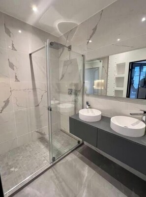 Ein modernes Badezimmer mit einer Duschkabine, zwei Waschbecken und einem großen Spiegel.