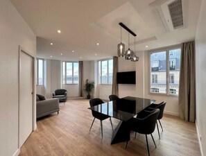 Ein modernes Wohnzimmer mit einem Glastisch, schwarzen Stühlen, einem grauen Sofa und einem großen Fenster mit Blick auf die Stadt.
