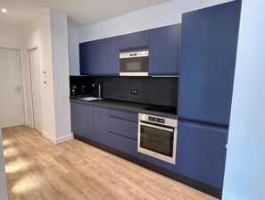 Eine moderne Küche mit dunkelblauen Schränken, einem Edelstahlbackofen und einer schwarzen Arbeitsplatte.