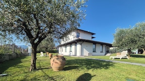 Une maison à l’extérieur blanc, dotée d’un patio couvert et d’une pelouse agrémentée d’un grand pot et d’un arbre.