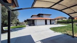 Un espace extérieur abrité avec une terrasse, une maison avec un toit en tuiles et un ciel bleu dégagé.