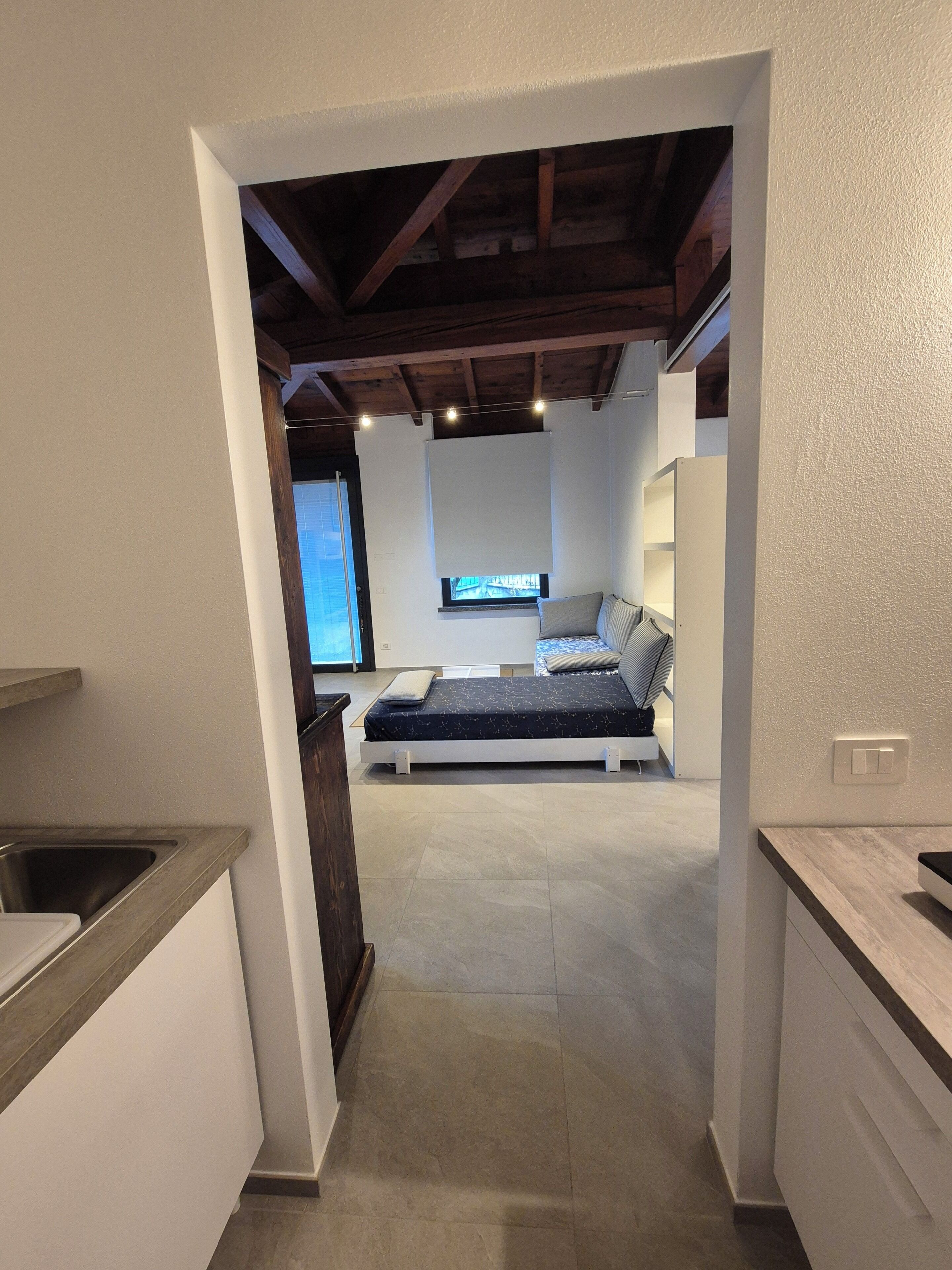 A modern interior with a kitchen area, a bed with a view, and a ceiling with exposed beams.
