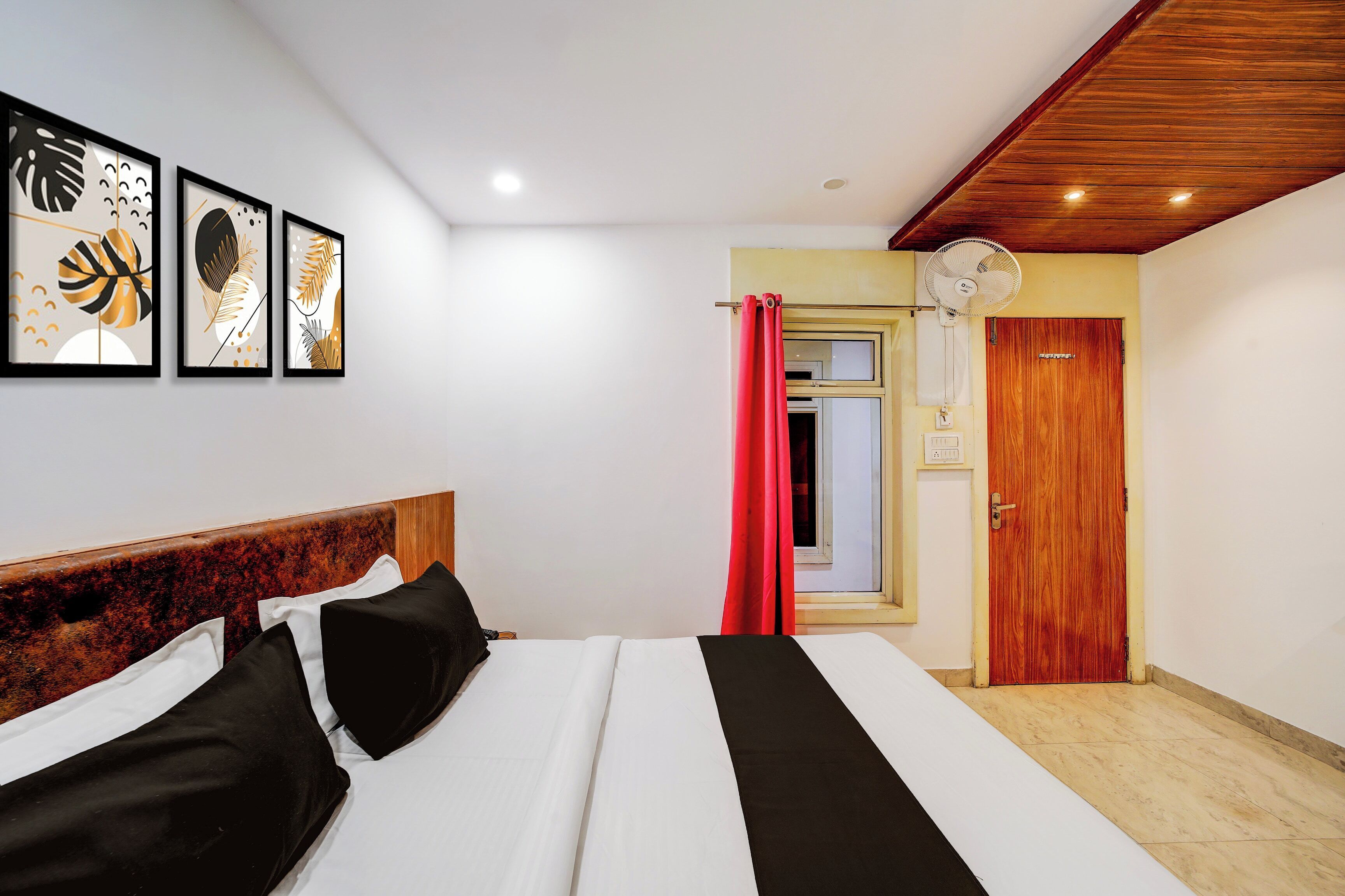 Ein Schlafzimmer mit einem Bett, einem Holzkopfende, einem Deckenventilator, einer Tür und Wandbildern.