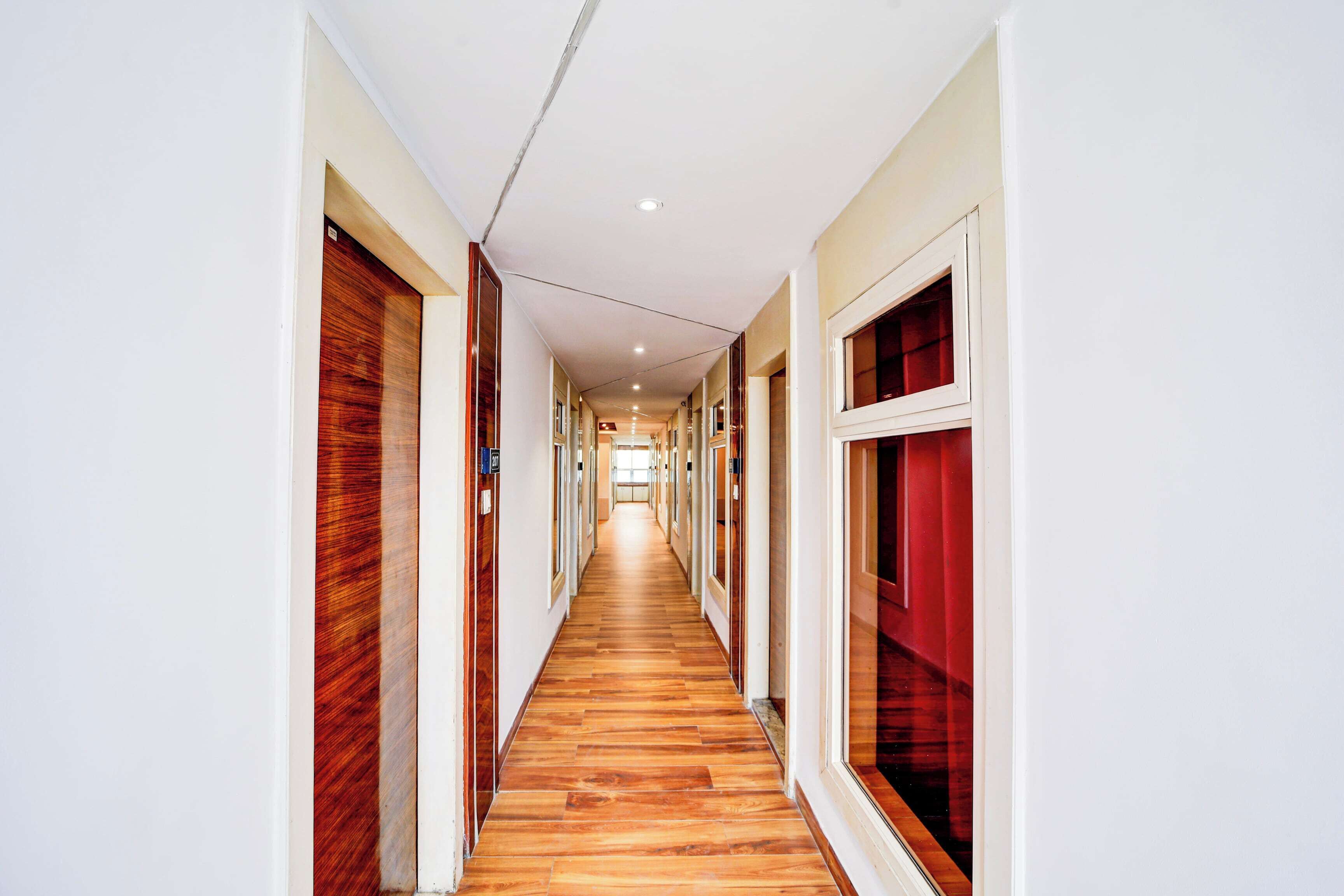 A long, narrow hallway with wooden flooring and white walls, leading to a bright room at the end.