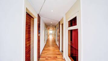 A long, narrow hallway with wooden flooring and white walls, leading to a bright room at the end.
