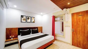 A hotel room with a bed, a wooden headboard, a bedside table with a vase, a red curtain, and a wooden wardrobe.