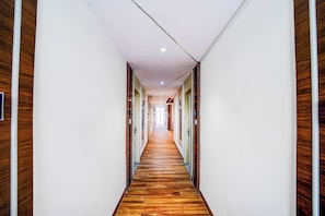 A long, narrow hallway with wooden flooring and white walls, leading to multiple doors.