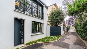 Una calle estrecha con un edificio moderno de dos pisos, una entrada con reja y un pequeño jardín.