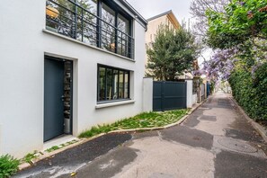 Eine enge Straße mit einem modernen, zweistöckigen Gebäude, einem befestigten Eingang und einem kleinen Garten.