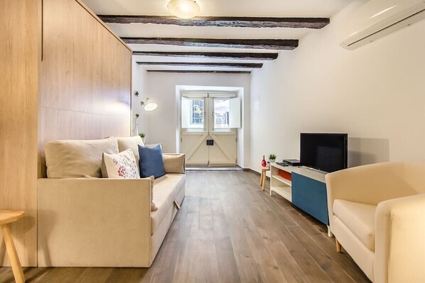 A modern living room with a sofa, TV, and a small table. - Brick Arch Studio With AC Alfama (Lisbon)