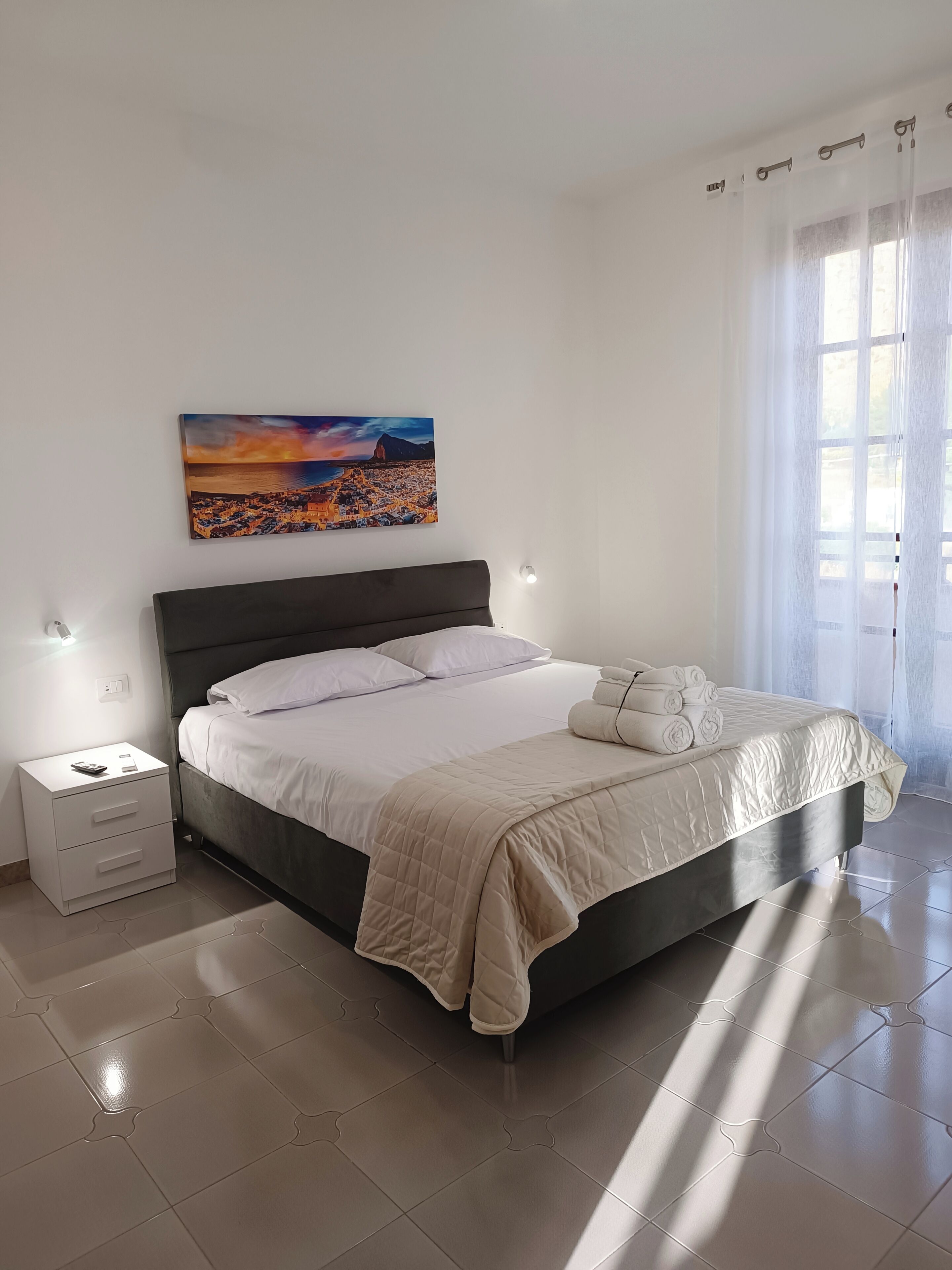 Ein modernes Schlafzimmer mit einem großen Bett, einem Nachttisch, einem Wandbild und einem Fenster mit Vorhängen.