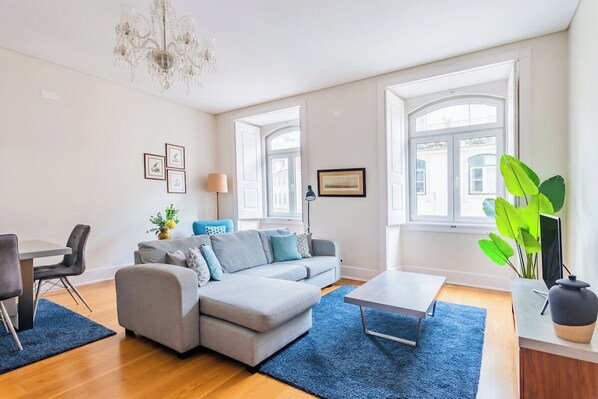 A modern living room with a sectional sofa, a coffee table, a dining area with a table and chairs, and large windows. - Downtown 75 Prestige in Baixa (Lisbon)