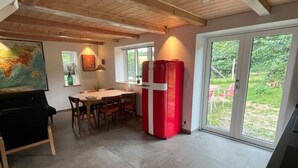 Eine Küche mit Esstisch, Stühlen, einem roten Kühlschrank und einem großen Fenster mit Blick auf Grünflächen.