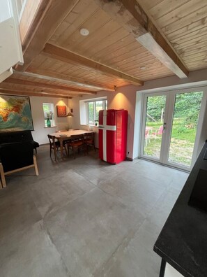 Eine Küche mit Esstisch, Stühlen, einem roten Kühlschrank und einem großen Fenster mit Blick auf Grünflächen.