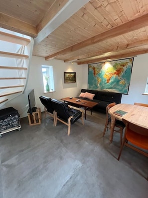 Et loftrum med skrå vægge, et stort verdenskort på væggen, en sort lædersofa, et træspisebord og en trappe med udsigt udad.