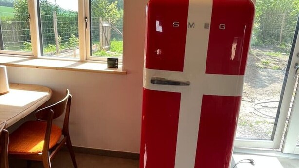 Eine kleine Küche mit einem roten und weißen Kühlschrank, einem Esstisch mit Stühlen und einem Fenster mit Blick auf einen Garten.