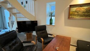 Ein Wohnzimmer mit Holztisch, zwei Ledersesseln, einem Fernseher und einem Bild an der Wand.
