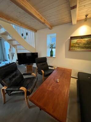 Ein Wohnzimmer mit Holztisch, zwei Ledersesseln, einem Fernseher und einem Bild an der Wand.