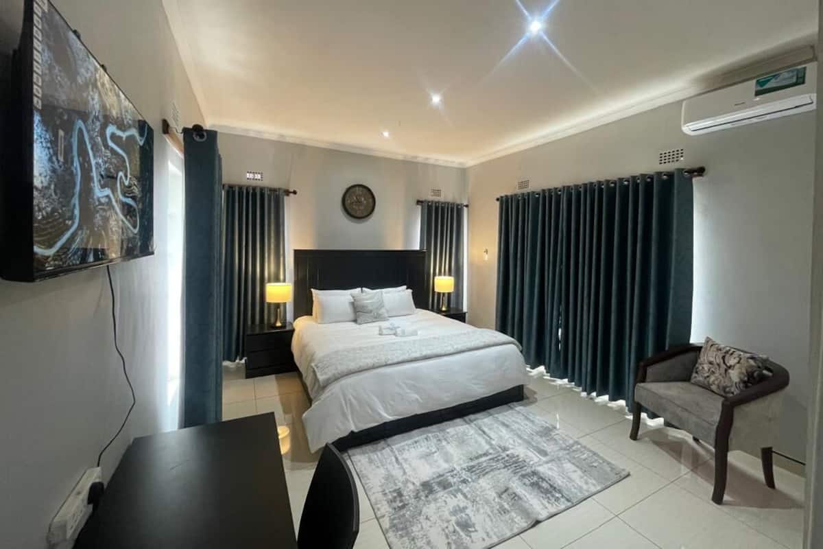 Una habitación de hotel moderna con una cama grande, lámparas de noche, un escritorio y un televisor en la pared.