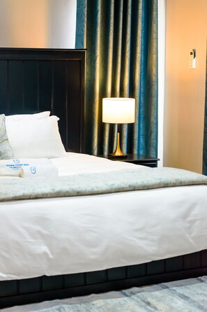 A hotel room with a bed, a nightstand, a lamp, and a curtain.