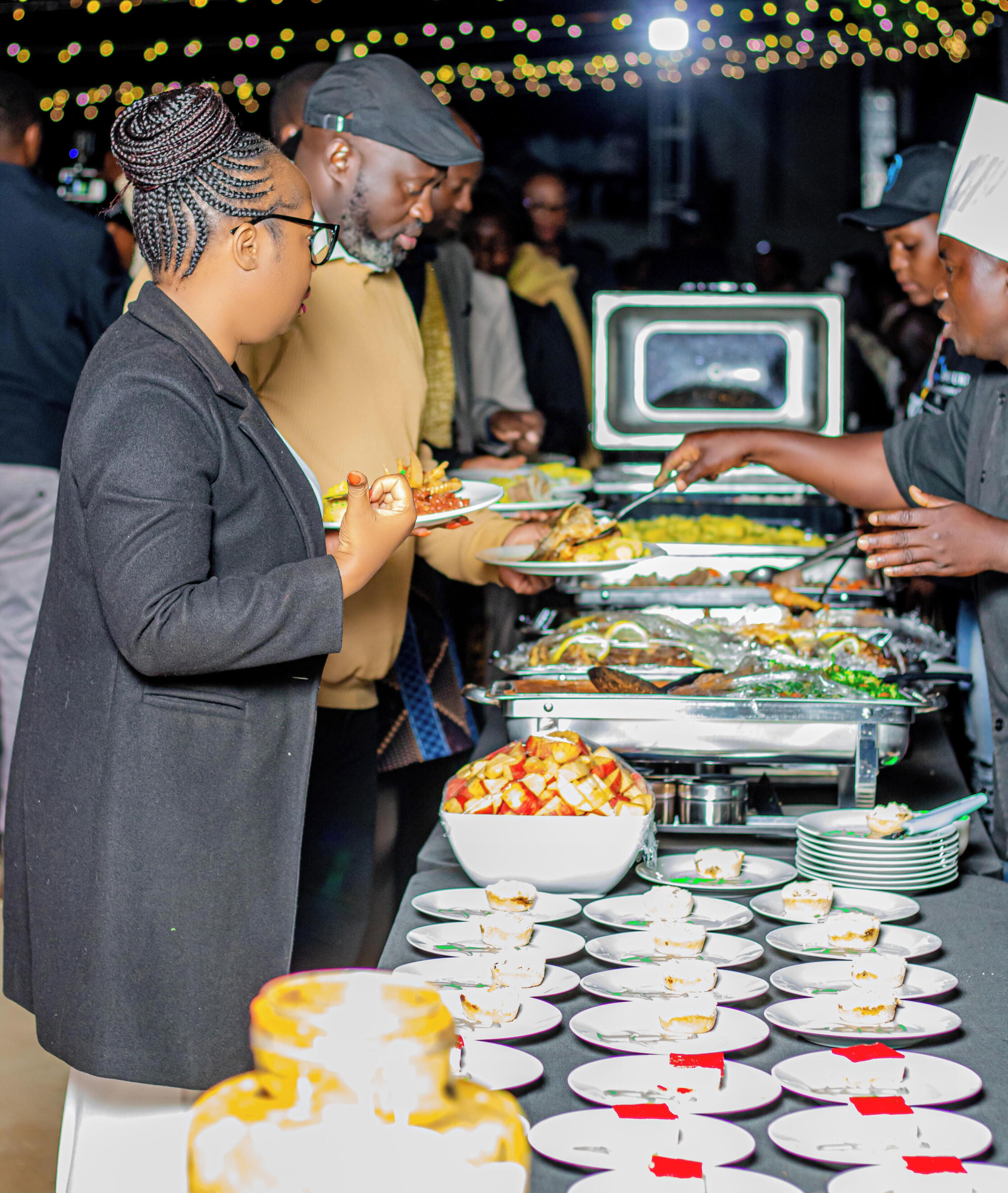 A buffet setup with various food items and a crowd of people.