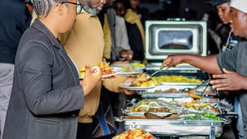 A buffet setup with various food items and a crowd of people.