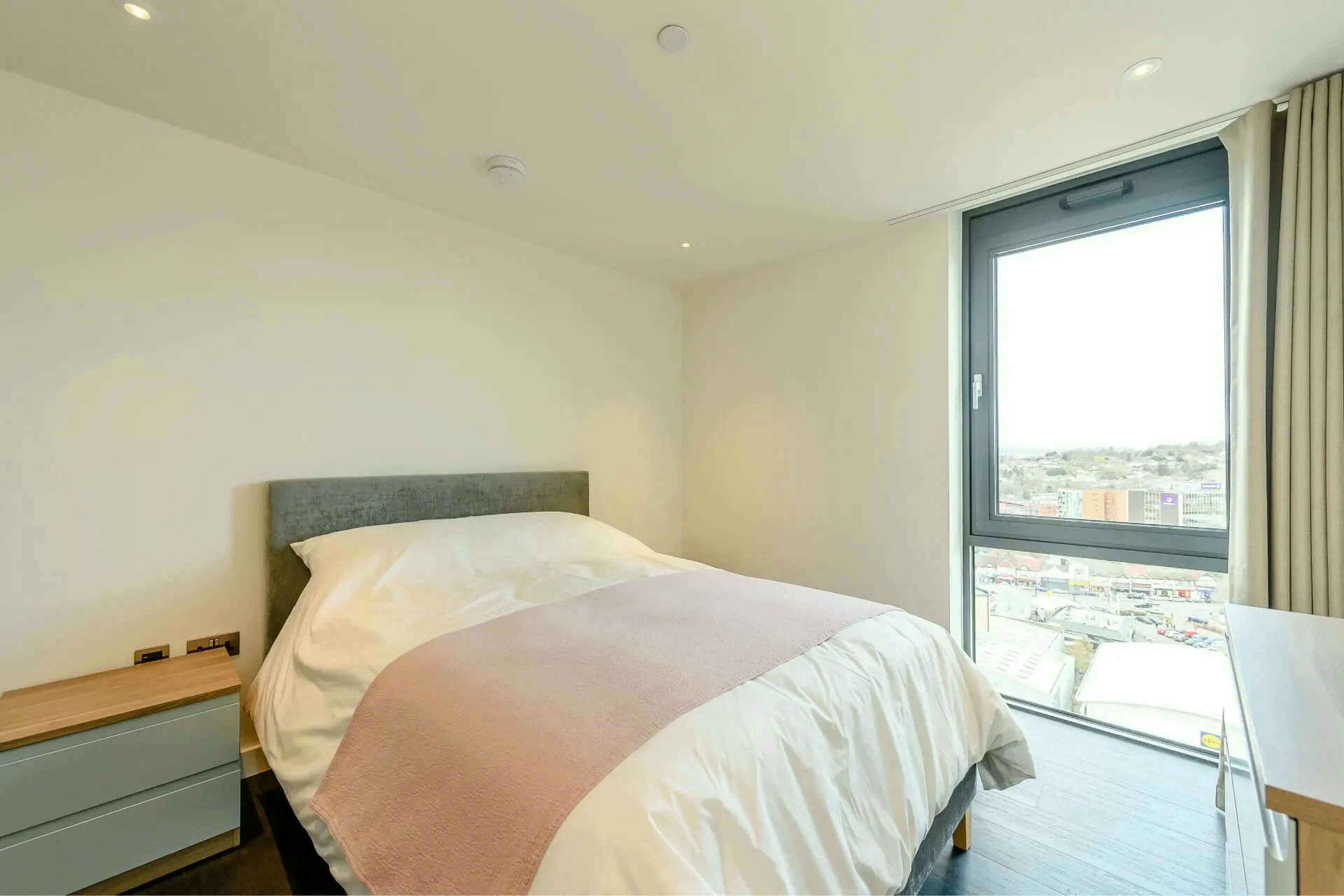 Habitación de hotel con cama, mesita de noche, ventana con vista a la ciudad y escritorio.