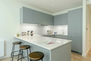 A modern kitchen with grey cabinets, a white countertop, and a central island with stools. - Landsby (Wembley)