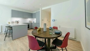 A modern kitchen with grey cabinets, a central island, and a dining area with a round table and red chairs. - Landsby (Wembley)