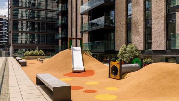 An outdoor play area with a slide, sand play area, and seating. - Landsby (Wembley)