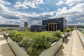 A modern building with a flat roof, surrounded by a well-maintained garden and a pedestrian walkway. - Landsby (Wembley)