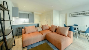 A modern living room with a sectional sofa, a dining table with chairs, and a kitchen area in the background. - Landsby (Wembley)