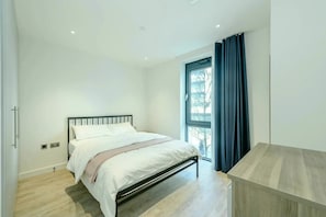 A bedroom with a bed, a window with curtains, and a wooden bench. - Landsby (Wembley)