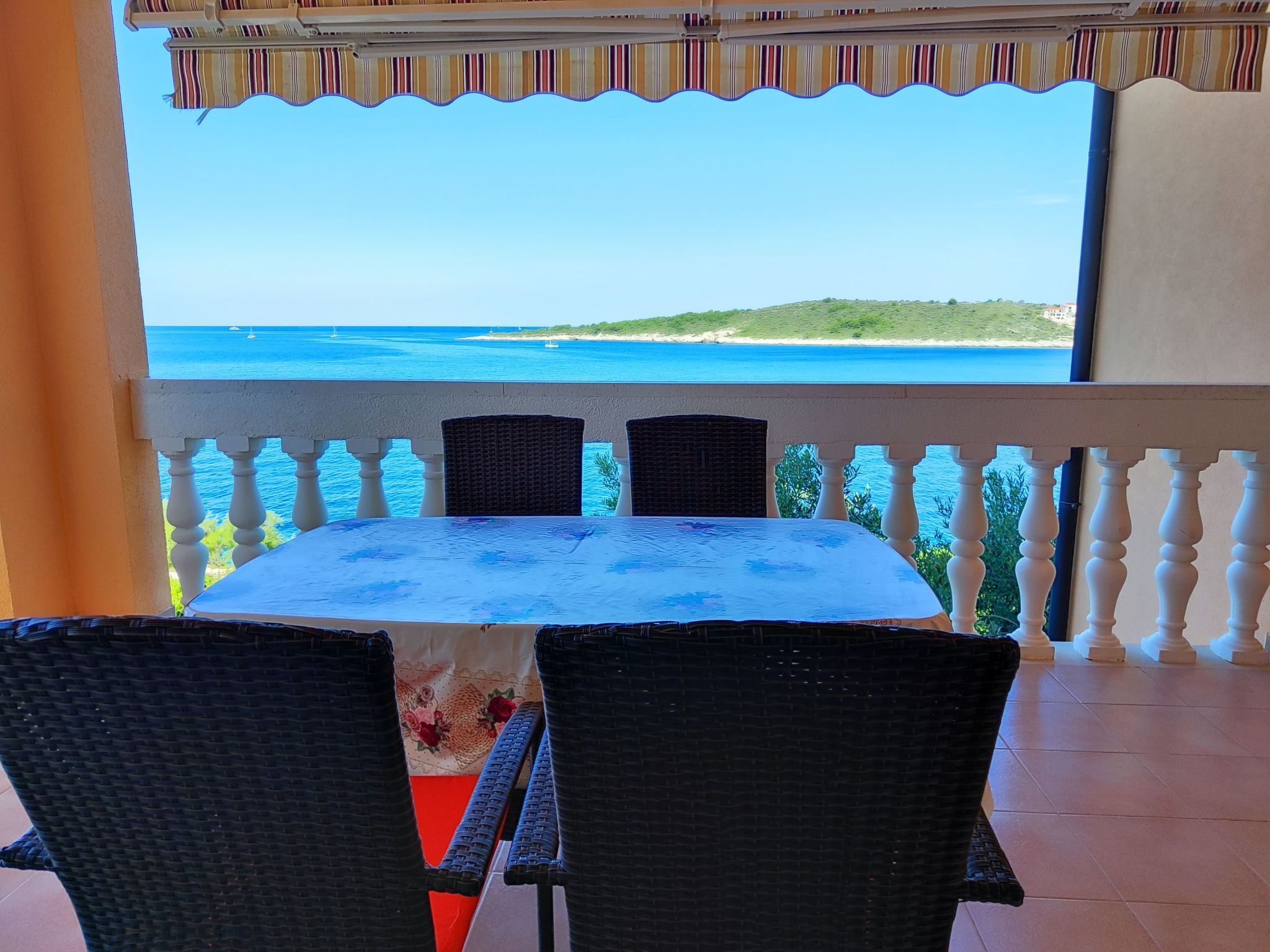 Une table ronde entourée de quatre chaises, sur un balcon donnant sur une plage.