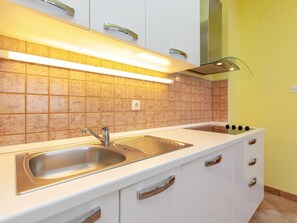 Eine moderne Küche mit Spüle aus Edelstahl, weißen Schränken und einer Rückwand aus quadratischen Fliesen.