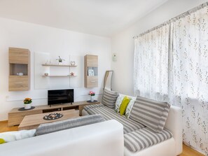 Ein modernes Wohnzimmer mit einer Couch, einem Fernseher, Holzregalen und einem Fenster mit floralen Vorhängen.