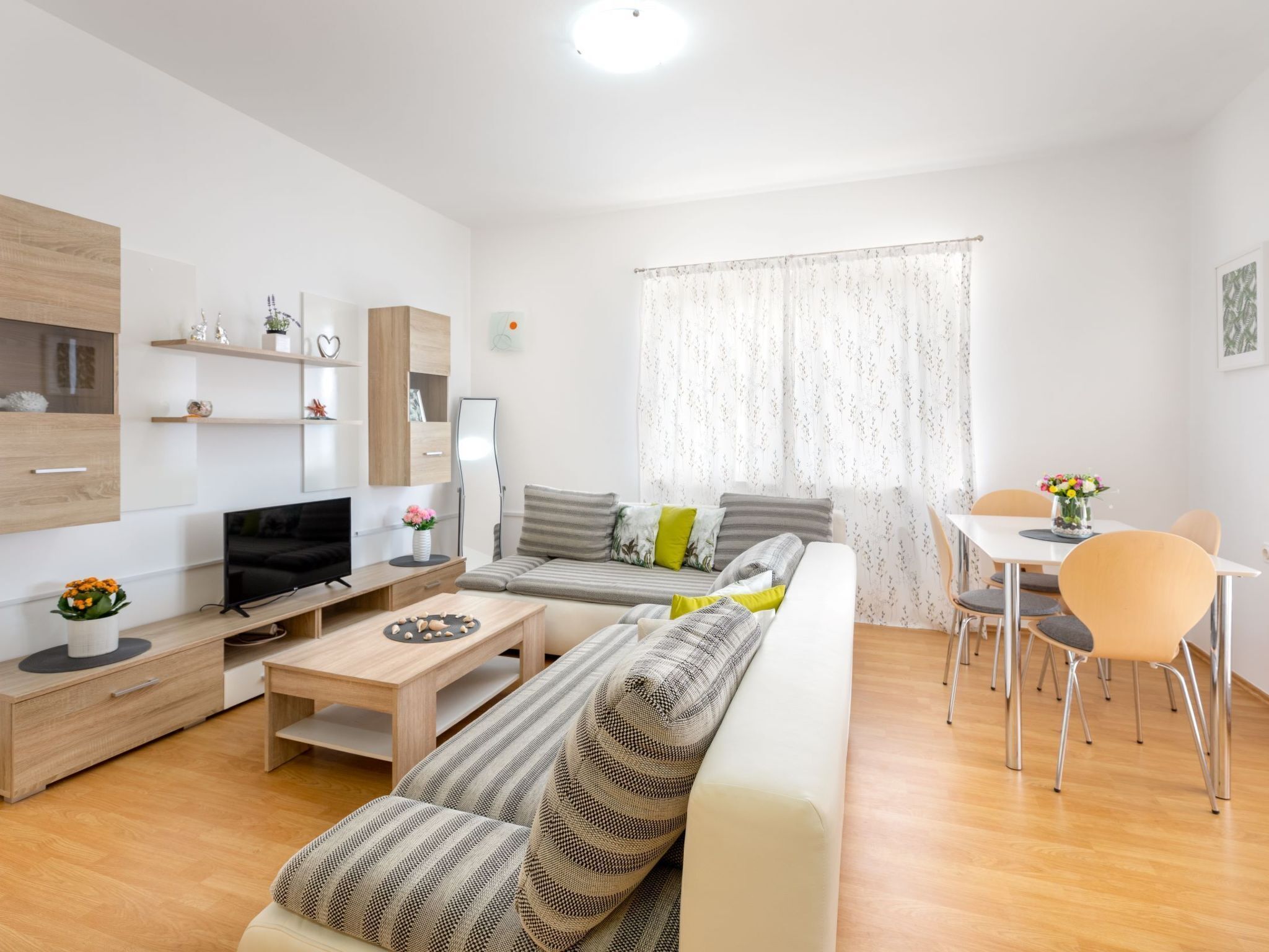 A modern living room with a sofa, coffee table, TV, and a dining area with chairs and a table.