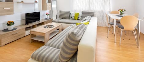 A modern living room with a sofa, coffee table, TV, and a dining area with chairs and a table.